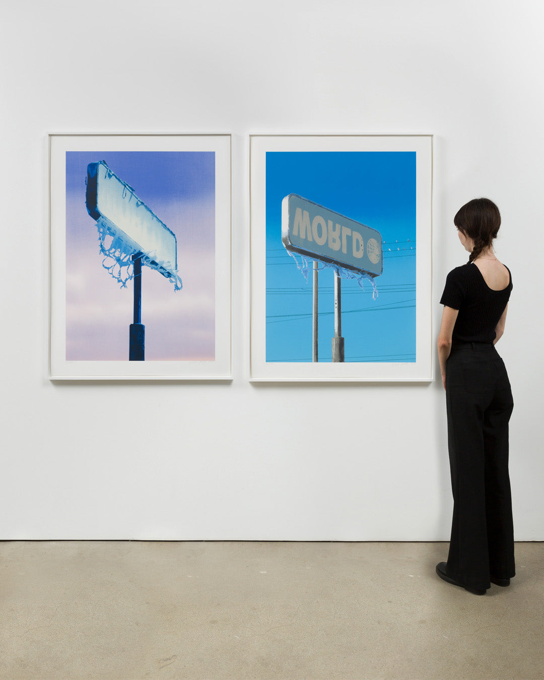 Both print editions by Sayre Gomez, World 1 and World 2, framed and hung in gallery wall with a person next to them to show scale. Installation view.